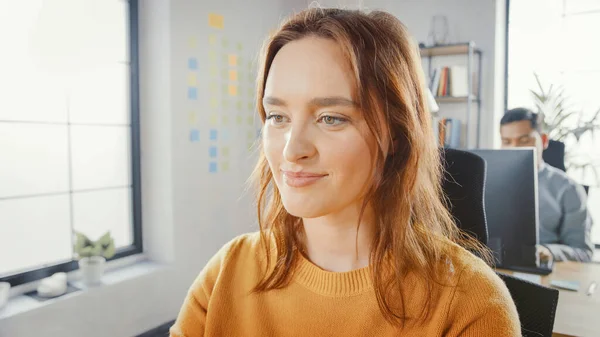 Porträtaufnahme der schönen jungen Spezialistin, die an ihrem Schreibtisch sitzt und am Desktop-Computer arbeitet. Vielfältiges und modernes Büro mit professionellen Mitarbeitern. — Stockfoto