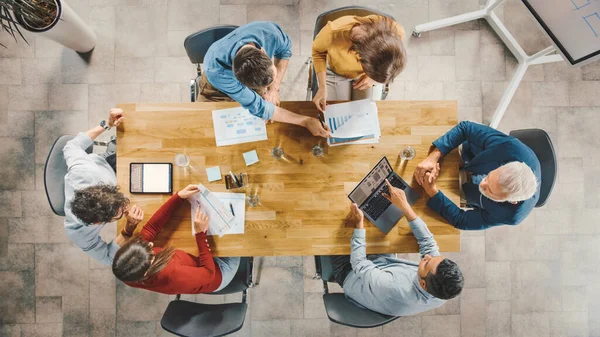 Dalam Startup Meeting Room Team of Entrepreneurs yang duduk di Conference Table Have Discussions, Solve Problems, Use Digital Tablet, Laptop, Share Documents with Statistics and Charts. Tampilan Atas — Stok Foto