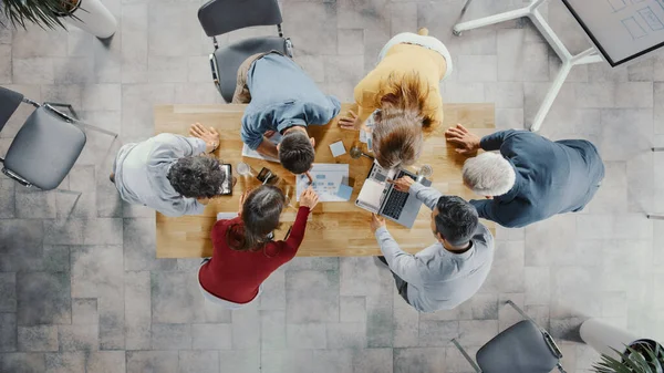 Startup Meeting Room: Team of Entrepreneurs Standing Around Conference Table Have Discussions, Solve Problems, Use Digital Tablet, Laptop, Share Documents with Statistics, Charts (dalam bahasa Inggris). Tampilan Atas Ditembak — Stok Foto