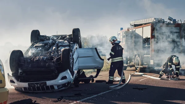 Команда рятувальних пожежників прибуває на місце аварійного дорожньо-транспортного пригодницького руху на своєму пожежному двигуні. Пожежники захоплюють їхнє обладнання, готують пожежні Хоссес і передачу з пожежної машини. — стокове фото