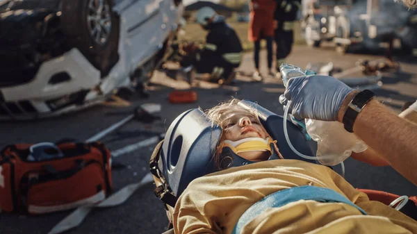Na miejscu wypadku samochodowego: ratownicy medyczni ratujący życie ofiary wypadku samochodowego leżącej na noszach. Słuchają bicia serca, stosują maskę tlenową i udzielają pierwszej pomocy — Zdjęcie stockowe