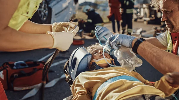 På bilolyckan Trafikolycka Scen: Paramedicin Rädda livet på en trafikolycka offer som ligger på bårar. De lyssnar på en Heartbeat, applicera Oxygen Mask och ge första hjälpen — Stockfoto