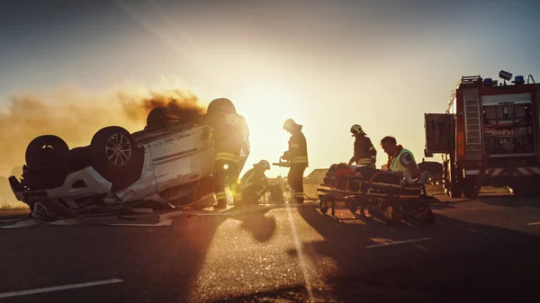 "On the Car Crash Traffic Accident: Paramedics and Firefighter Rescue" Першу допомогу посідає жіноча шкідниця. Пожежники використовують гідравлічні радари, щоб відкрити автомобіль — стокове фото