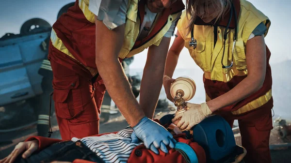 On the Car Crash Traffic Accident Scene: Paramedics Saving Life of a Female Victim who is Lying on Stretchers. They Apply Oxygen Mask, Do Cardiopulmonary Resuscitation CPR and Perform First Aid — Stock Photo, Image