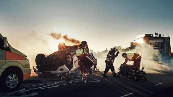 On the Car Crash Traffic Accident Scene: Rescue Team of Firefighters Pull Female Victim out of Rollover Vehicle, They Use Stretchers Carefully, Hand Her Over to Paramedics who Perform First Aid