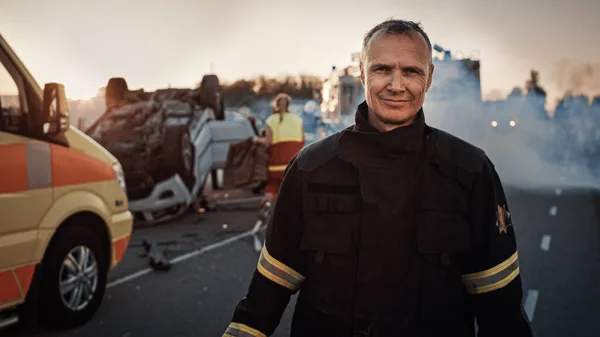 Porträtt av den modiga brandmannen som ler mot kameran. I bakgrunden modiga hjältar Ambulans och brandmän räddningsteam bekämpa brand, rök och rädda människors liv — Stockfoto