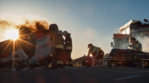 Autounfall: Rettungssanitäter und Feuerwehrleute retten eingeklemmte Passagiere in einem Überschlagfahrzeug Sanitäter bereiten Erste-Hilfe-Ausrüstung vor. Feuerwehr setzt hydraulischen Schneidspreizer ein, um Fahrzeug zu öffnen — Stockfoto