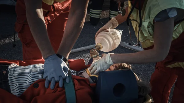 On the Car Crash Traffic Accident Scene: Paramedics Saving Life of a Female Victim who is Lying on Stretchers. Ze passen zuurstofmasker toe, doen cardiopulmonale reanimatie en voeren eerste hulp uit. — Stockfoto