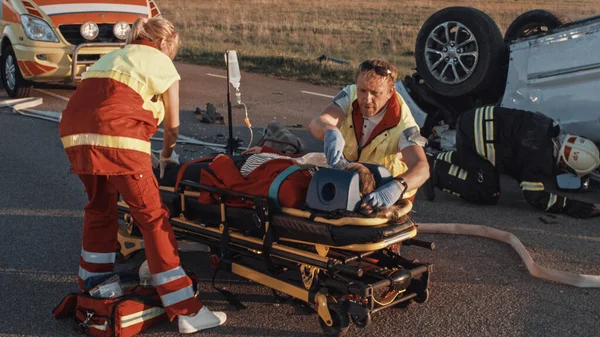 Na miejscu wypadku samochodowego: ratownicy medyczni ratujący życie kobiety, która leży na noszach. Stosują maskę tlenową, wykonują resuscytację serca i pierwszą pomoc. — Zdjęcie stockowe