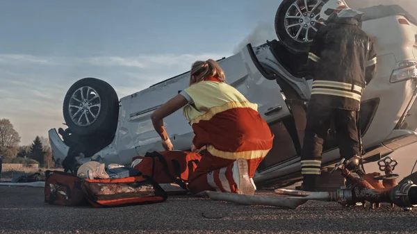 Nehoda při autonehodě: Záchranáři a hasiči Záchranáři Uvězněni v hořícím vozidle Rollover. Doktoři připravte první pomoc. Záběr pod úhlem — Stock fotografie