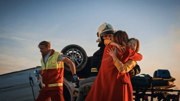 Aufnahme der süßen Mutter, die ihre kleine Tochter umarmt, die Opfer eines schrecklichen Unfalls wurde. Im Hintergrund Autounfall Verkehrsunfälle Mutige Sanitäter und Feuerwehrleute retten Leben — Stockfoto