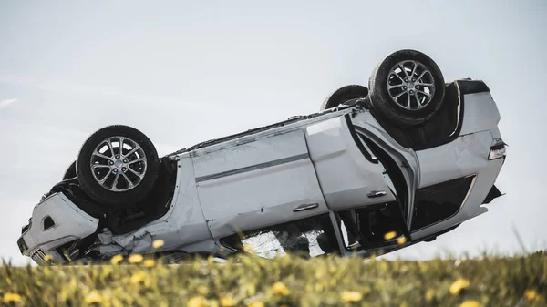 Strašlivá dopravní nehoda, Rollover kouřící a hořící vozidlo ležící na střeše uprostřed silnice po srážce. Denní havarijní scéna s těžce poškozeným autem. — Stock fotografie