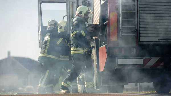 Einsatzkräfte der Feuerwehr treffen mit ihrem Löschfahrzeug am Unfallort ein. Feuerwehrmänner greifen nach Werkzeug, Ausrüstung und Ausrüstung aus Feuerwehrauto, eilen zu Verletzten, Verschütteten — Stockfoto