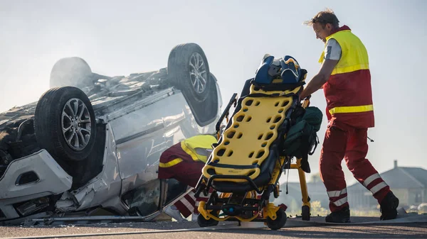 Paramedici en brandweerlieden arriveren op de auto-ongeluk plaats delict. Professionals Prepairing Stretchers voor redding verwond slachtoffer gevangen in roll-over voertuig. — Stockfoto