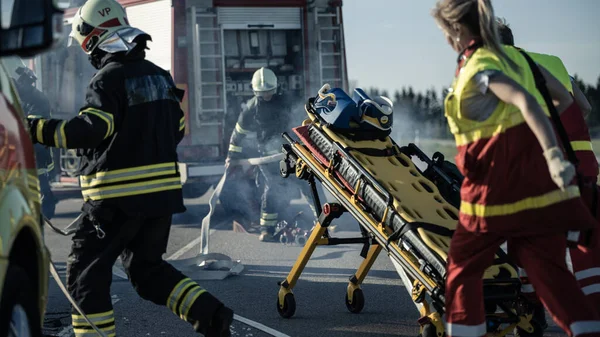 En la escena del accidente de tráfico: paramédicos y bomberos rescatan a las víctimas heridas atrapadas en el vehículo. Los médicos usan camillas, realizan primeros auxilios. Bomberos agarran el equipo de Fire Engine —  Fotos de Stock