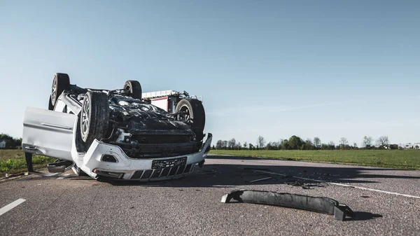 Horrific Traffic Accident Rollover Smoking and Burning Vehicle Liggend op het dak in het midden van de weg na de botsing. Overdag Crash Scene met beschadigde auto. Lage hoek schot — Stockfoto