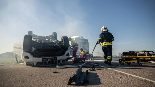 No acidente de carro Cena de acidente de trânsito: paramédicos e bombeiros salvam vítimas feridas presas no veículo. Bombeiros preparam mangueiras de incêndio . — Fotografia de Stock