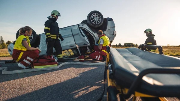On the Car Crash Traffic Accident Scene: paramedici en brandweerlieden redden gewond slachtoffer gevangen in het voertuig. Extricate Persoon met behulp van Stretchers, Geef EHBO en vervoer ze naar het ziekenhuis — Stockfoto