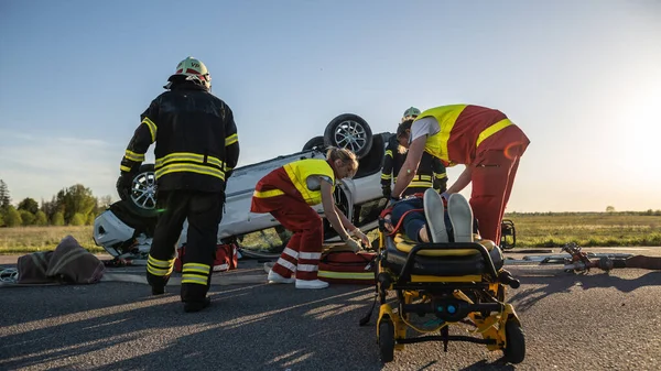 On the Car Crash Traffic Accident Scene: Paramedics Saving Life of a Female Victim who is Lying on Stretchers. Ze luisteren naar een hartslag, brengen zuurstofmasker aan en geven EHBO. Achtergrond Brandweerlieden — Stockfoto