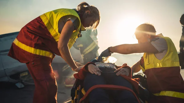 No acidente de carro Cena de acidente de trânsito: paramédicos salvando a vida de uma vítima feminina que está deitada em maca. Eles ouvem um batimento cardíaco, aplicam máscara de oxigênio e dão primeiros socorros. Contexto Bombeiros — Fotografia de Stock