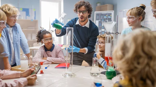 小学理科化学课堂:教师向儿童群体展示化学反应实验.在Beaker中混合化学物以得到反应。感兴趣地等待的儿童. — 图库照片
