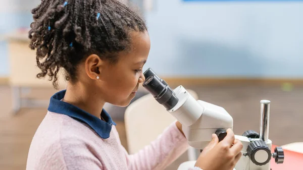 Retrato de una colegiala inteligente mirando bajo el microscopio. En el aula de la escuela primaria linda chica utiliza microscopio. Programa STEM de Ciencia, Tecnología, Ingeniería y Matemáticas —  Fotos de Stock