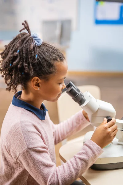 Portrait of Smart Little Schoolgirl Looking Under the Microscope. In Elementary School Classroom Cute Girl Uses Microscope. STEM science, technology, engineering and mathematics Education Program