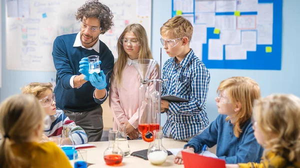 Szkoła Podstawowa Nauka Klasa: Entuzjastyczny Nauczyciel Wyjaśnia Chemię Różnorodnej Grupie Dzieci, Pokazuje Jak Mieszać Chemikalia W Zlewkach. Dzieci wyglądają z zainteresowaniem i rozmową — Zdjęcie stockowe