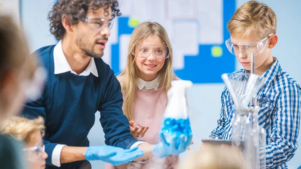 Grundskola Science Classroom: Entusiastisk lärare förklarar kemi för olika grupper av barn, visar dem hur man blandar kemikalier i bägare. Barn använder digitala surfplattor och pratar — Stockfoto
