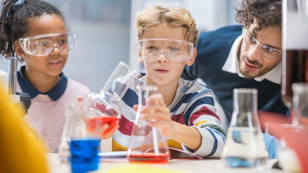 Basisschool Science Classroom: Enthousiaste leraar legt scheikunde uit aan diverse groep kinderen, Little Boy Mixes Chemicals in Beakers. Kinderen leren met rente — Stockfoto