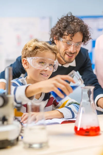 Grundskolan Science Classroom: Lilla pojken blandar kemikalier i bägare, Entusiastisk lärare hjälper med kemi vetenskap till ett barn. Barn lär sig med intresse — Stockfoto