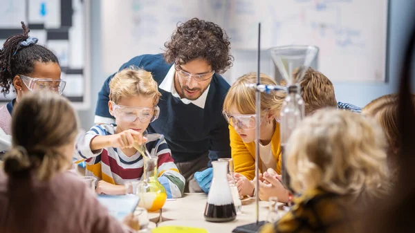 Aula de Ciencias de la Escuela Primaria: Profesor Entusiasta Explica Química a Diverso Grupo de Niños, Niño Pequeño Mezcla Químicos en Beakers. Niños aprenden con interés —  Fotos de Stock