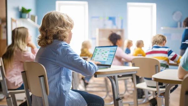 Basisschool Science Class: Little Boy maakt gebruik van Laptop met Screen Showing Programming Software. Fysica Docent legt les uit aan een gevarieerde klas vol slimme kinderen. Over de schouder geschoten.. — Stockfoto