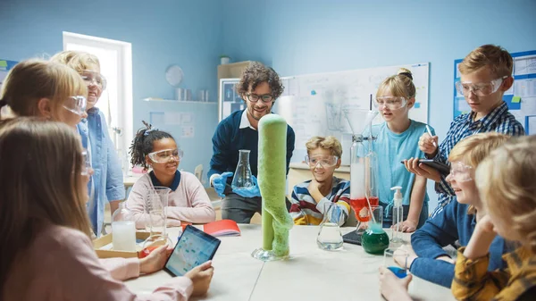 Grundskola vetenskap kemi Klassrum: Entusiastiska lärare visar roliga kemiska reaktioner Experiment till grupp av barn. Blandning kemikalier i bägare så de skjuter skum elefant tandkräm — Stockfoto