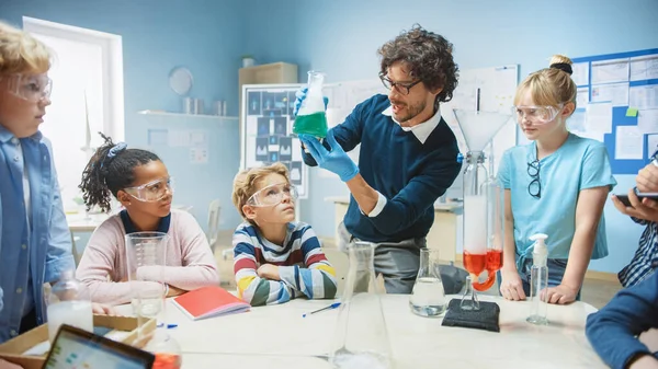 小学理科化学课堂:教师向儿童群体展示化学反应实验.在Beaker中混合化学物以得到反应。儿童使用数码制表电脑 — 图库照片