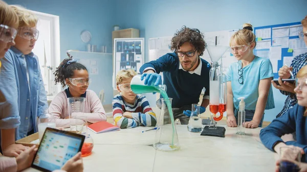 초등 학교 화학 교실: 교사 화학 반응 실험을 어린이 그룹에 보여 주다. 반응을 얻기 위해 비커에 있는 화학 물질을 혼합 합니다. 어린이들이 디지털 태블릿 컴퓨터를 사용하다 — 스톡 사진