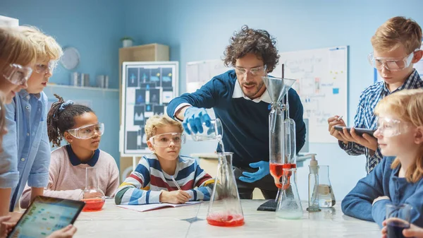 Класс химии начальной школы: Энтузиастичный учитель преподает различные группы детей показывает научный эксперимент реакции путем смешивания химических веществ в стакане, так что они стреляют пены слона зубная паста — стоковое фото