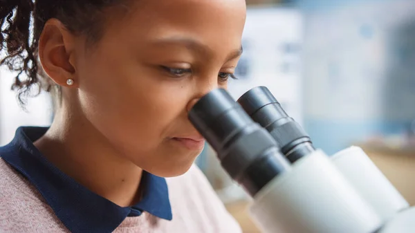 Retrato de una colegiala inteligente mirando bajo el microscopio. En el aula de la escuela primaria linda chica utiliza microscopio. Programa STEM de Ciencia, Tecnología, Ingeniería y Matemáticas — Foto de Stock