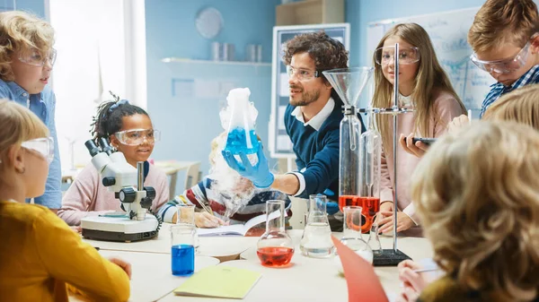 İlköğretim Okulu Bilim Sınıfı: Coşkulu Öğretmen Kimyayı Farklı Çocuklar Grubu 'na Açıklıyor, Kimyasalları Şişelerde Nasıl Karıştıracaklarını Gösteriyor. Çocuklar Dijital Tablet Bilgisayarları Kullanır ve Konuşur