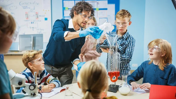 초등 학교의 과학 교실: 학생들의 다양 한 그룹에게 화학을 설명하는 열정적 인 교사, 그들에게 비버에 있는 화학 물질을 혼합하는 방법을 보여준다. 어린이들이 디지털 태블릿 컴퓨터와 대화를 사용하는 방법 — 스톡 사진