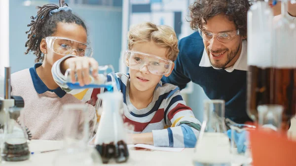 Szkoła podstawowa Nauka Klasa: Mały chłopiec miesza chemikalia w zlewkach. Entuzjastyczny Nauczyciel Wyjaśnia Chemię Zróżnicowanej Grupie Dzieci. Dzieci uczą się z zainteresowaniem — Zdjęcie stockowe
