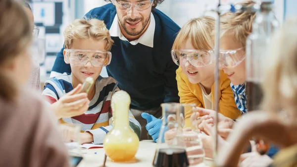Grundskola Science Classroom: Entusiastisk lärare förklarar kemi för olika grupper av barn, små pojke blandar kemikalier i bägare. Barn lär sig med intresse — Stockfoto