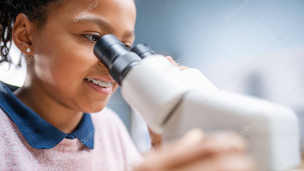 Portrait of Smart Little Schoolgirl Looking Under the Microscope. In Elementary School Classroom Cute Girl Uses Microscope. STEM science, technology, engineering and mathematics Education Program