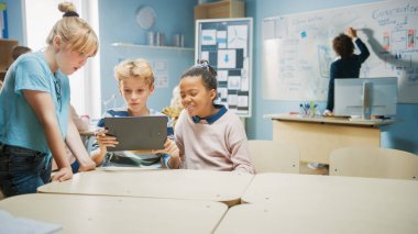 İlköğretim Okulu Bilgisayar Bilimi Sınıfı: İki Kız ve Erkek Artırılmış Gerçeklik Yazılımı ile Dijital Tablet Bilgisayar Kullanıyor, Heyecanlı, Merakla Dolu, Merak Dolu. STEM 'deki Çocuklar, Oynamak, Öğrenmek