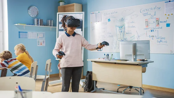 Clase primaria de ciencias de la computación: Linda chica con auriculares de realidad aumentada y el uso de controladores aprende lecciones de realidad virtual Emocionado, curioso e interesado en el conocimiento —  Fotos de Stock