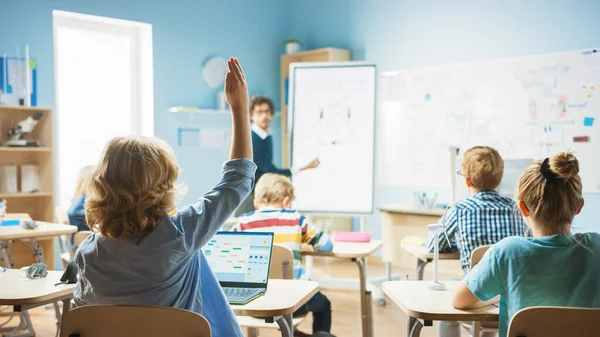 Nauczyciel fizyki w szkole podstawowej wykorzystuje interaktywną tablicę cyfrową, aby pokazać klasie pełnej inteligentnych dzieci, jak działa generator. Klasa naukowa, Kid podnosi rękę z odpowiedzią — Zdjęcie stockowe