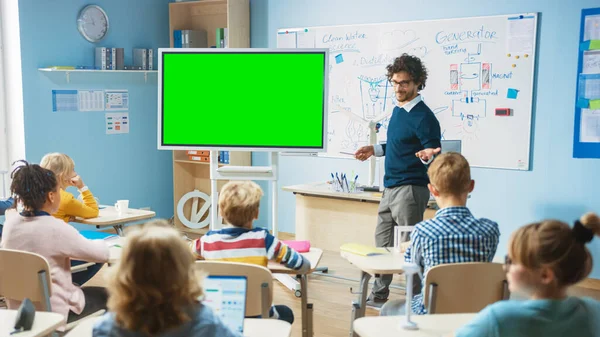 Elementary School Physics Teacher Uses Interactive Digital Whiteboard With Green Screen Mock-up Template. He Leads Lesson to Classroom full of Smart Diverse Children. Science Class with Kids Listening