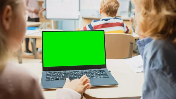 Általános Iskolai Tudományos Osztály: Over the Shoulder Little Boy and Girl Használja Laptop zöld képernyős Mock-up Template egy kijelzőn. A fizika tanár elmagyarázza a leckét egy sokszínű osztálynak, tele okos gyerekekkel. — Stock Fotó