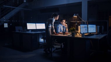 Hırslı ve kendinden emin işadamı Masaüstü Bilgisayarı Kullanıyor, Onun Kadın Proje Yöneticisi Özel Görevleri, Hesaplama ve Stratejik Hareketleri Açıklıyor. Büyük Kurumsal Ofiste Gece Geç Saatlere Kalanlar