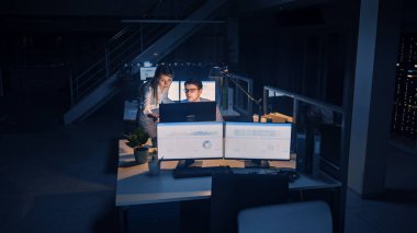 Hırslı ve kendinden emin işadamı Masaüstü Bilgisayarı Kullanıyor, Onun Kadın Proje Yöneticisi Özel Görevleri, Hesaplama ve Stratejik Hareketleri Açıklıyor. Profesyonel İnsanlar Büyük Ofiste Gece Geç Saatlere Kadar Çalışıyor